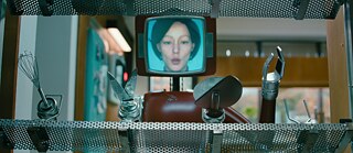 Cassandra - a dark red robot with an attached tube screen showing a white woman with neck-length hair views sharp kitchen utensils that attach to her arms.