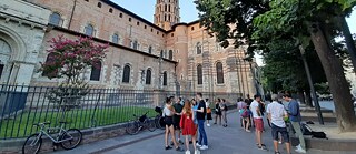 Des personnes discutent sous des arbres à côté de l'église Saint Sernin à Toulouse.