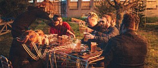 A group of people sitting outdoors at a table, enjoying drinks together. The image has a double-exposure effect.