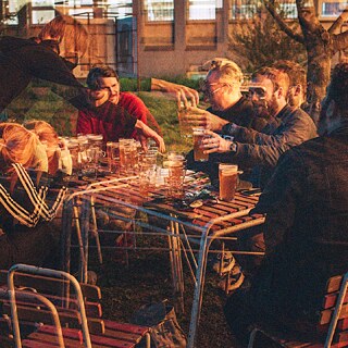 A group of people sitting outdoors at a table, enjoying drinks together. The image has a double-exposure effect.