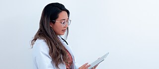 A doctor in a white coat reviews information on a tablet against a plain background. © © pixabay Doctor Reviewing Information on Tablet