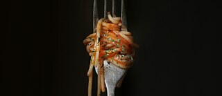 A close-up of a fork twirled with spaghetti in tomato sauce, garnished with herbs, against a black background. &copy; © Unsplash Spaghetti on a Fork