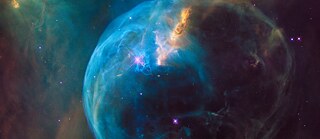 A vibrant image of the Bubble Nebula, showcasing a glowing blue sphere of gas and dust surrounded by swirling clouds of orange and green, with stars scattered throughout the dark cosmic background. © © Unsplash The Bubble Nebula