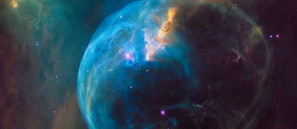 A vibrant image of the Bubble Nebula, showcasing a glowing blue sphere of gas and dust surrounded by swirling clouds of orange and green, with stars scattered throughout the dark cosmic background.