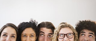 Nahaufnahme der Gesichter mehrerer, junger Leute, die alle verschmitzt nach oben sehen.