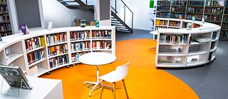 Die Bibliothek des Goethe-Instituts Warschau mit ihrem runden, orangefarbenen Boden und den weißen Regalen voller Bücher.