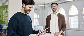 Zwei Männer stehen vor einem Schreibtisch im Goethe-Institut und führen ein Gespräch.