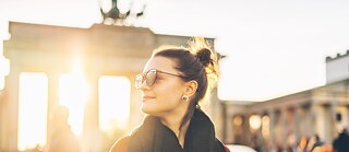 Eine Frau mit Sonnenbrille posiert vor dem Brandenburger Tor und hebt das Wahrzeichen der Stadt hervor.
