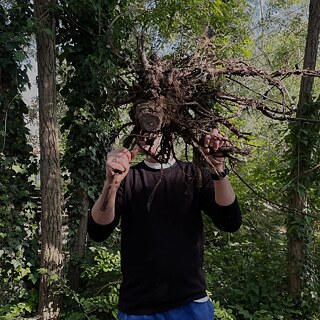 A man in the forest holding a root in front of his face.