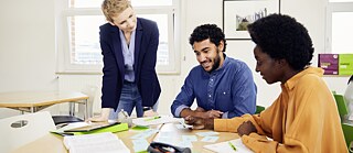 Leon und Whitney im Sprachkurs am Goethe-Institut. Deutschübung mit Lehrkraft. Die Kursteilnehmer machen gemeinsam Sprachübungen mit den Lernkarten. Die Lehrerin betreut die Übung.