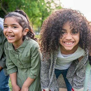 Einige Grundschüler bilden eine Gruppe. Sie legen die Hände auf die Knie und lachen in die Kamera.