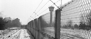 A metal fence fitted with barbed wire and a watchtower on the former death strip at the inner-German border, photographed near Salzwedel in February 1990. Some remains of the fortifications can still be visited to this day.