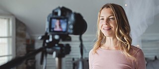 Eine Frau macht zu Hause ein Live-Streaming für die Sozialen Netzwerke. Blick von der Seite auf Kamera und Frau.