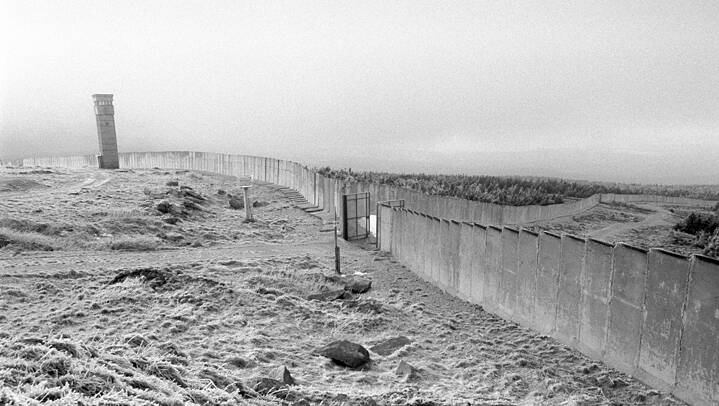 Schwarz weiß Bild von der innerdeutschen Grenze. Man sieht einen Turm, Mauern und einen Wald. 