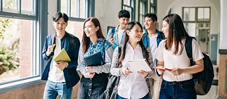 Young people walk through a university hallway and talk to each other.