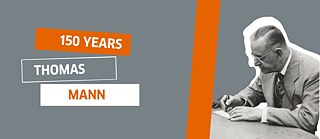 Thomas Mann schreibend an einem Tisch sitzend