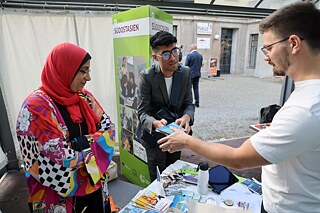 Three people stand around a table with information material