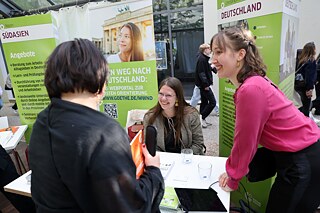 Three women chat at the information table about the offers from Germany