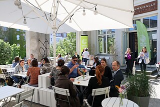 Personen sitzen im Freien an Tischen und unterhalten sich