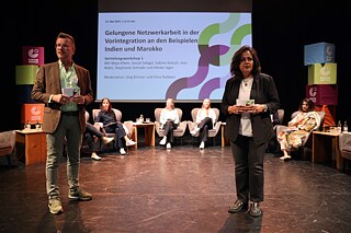 Sechs Personen sitzen und zwei stehen auf der Bühne und diskutieren