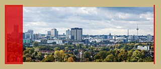 Man sieht die Skyline Essens bei bewölktem Himmel. Davor liegt ein Gebiet mit vielen Bäumen und vereinzelt Häusern.