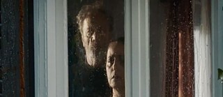 Ein Mann und eine Frau an einer verregneten Glasscheibe