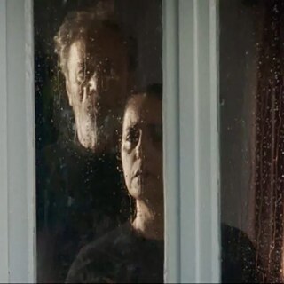 Ein Mann und eine Frau an einer verregneten Glasscheibe