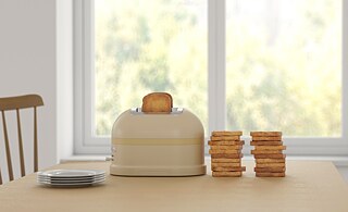 Ein Toaster steht auf einem Tisch, daneben sind mehrere Toastbrote aufeinandergestapelt. Im Hintergrund ein Fenster raus ins Grüne. 