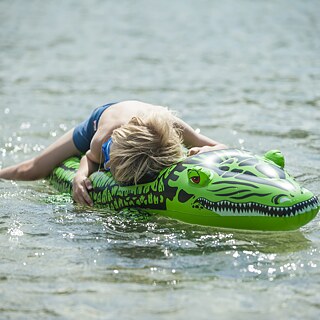 Ein Junge liegt auf einem aufblasbaren Krokodil im Wasser.