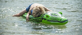 Ein Junge liegt auf einem aufblasbaren Krokodil im Wasser.