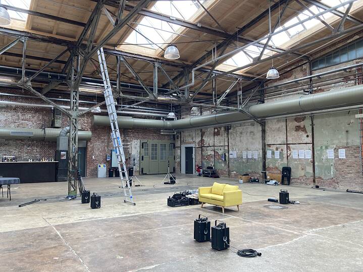 Eine Halle im Garagen-Campus mit verschiedenen Geräten; in der Mitte gibt es eine hohe Leiter und ein gelbes Sofa