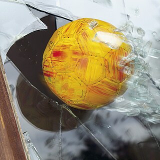 Ein Ball fliegt durch eine Fensterscheibe.