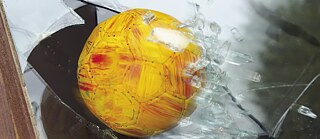 Ein Ball fliegt durch eine Fensterscheibe.