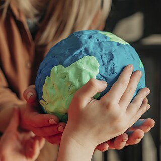 Hände halten eine Erdkugel aus Knetmasse.