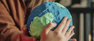 Hände halten eine Erdkugel aus Knetmasse.