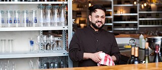 Ein Kellner steht an der Bar in einem Restaurant und trocknet Gläser ab.