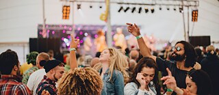 Unge mennesker danser foran en scene ute på en musikkfestival.