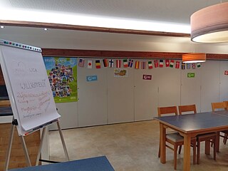 Ein Zimmer, ausgestattet mit Tischen und Stühlen, einer Flipchart, Plakaten und Flaggen aus vielen Ländern