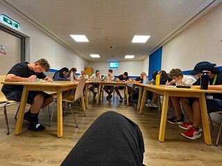 Jugendliche sitzen an in U-Form angeordneten Tischen und lernen.