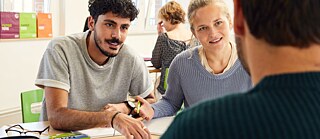 Eine heterogene Gruppe von Schüler*innen, die an einem Tisch im Klassenzimmer sitzen und aktiv an einer Gruppenaktivität teilnehmen