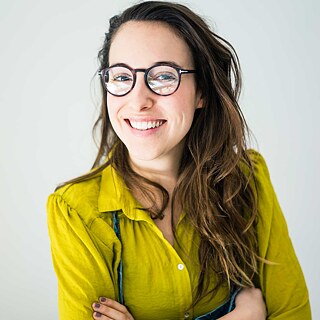 Eine Frau, die eine gelbe Bluse trägt, sieht lächelnd in die Kamera.