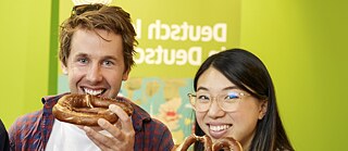 Ein Trio von Menschen, das stolz riesige Brezeln präsentiert, dabei lächelt und einen unbeschwerten Moment teilt