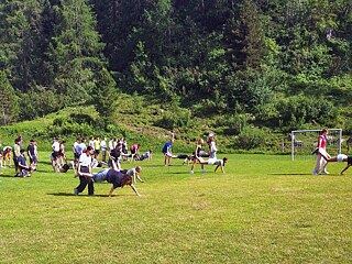 Jugendliche auf einer Wiese beim Schubkarrenrennen