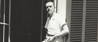 Un homme en vêtements estivaux appuyé contre la porte ouverte d'une maison