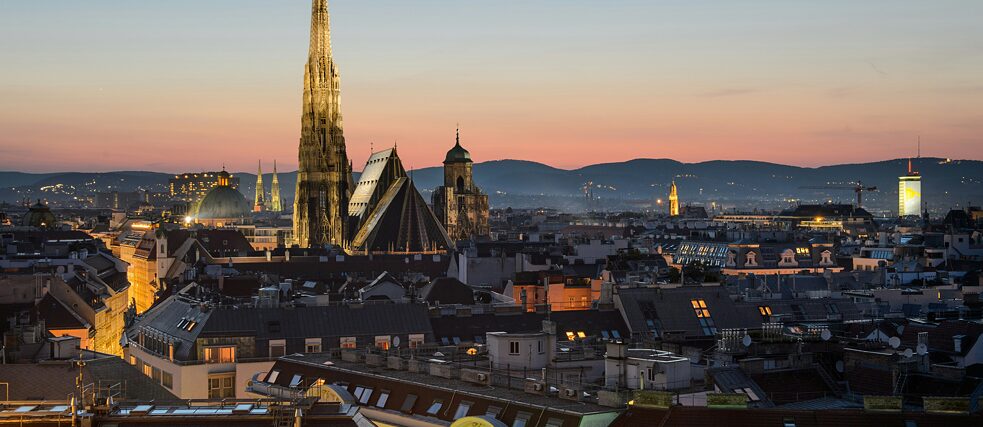 Cityscape of Vienna at sunset with St. Stephen's Cathedral prominently lit in the center.