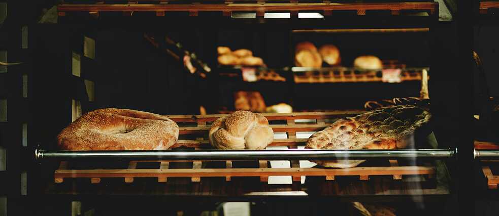 Assorted loaves of bread displayed on wooden shelves in a bakery.