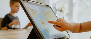 A child in the background, another child's hand on a tablet