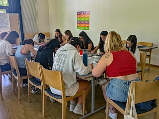 Jugendliche sitzen an einem Tisch, sie basteln und malen.