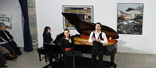 Ein Mann und eine Frau singen vor einem Klavier.