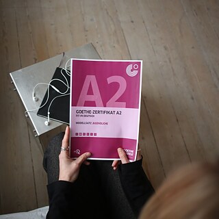Blick von oben auf eine Deutschlehrerin, die ein Goethe-Zertifikat A2 in der Hand hält.